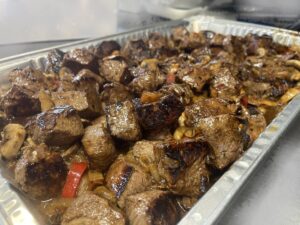 Marinated tenderloin steak tips grilled with seasoning and onions, peppers and mushrooms in a large foil pan , ready to serve to your party of up to 25 people